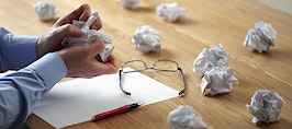 A frustrated man crumpling up paper drafts of writing