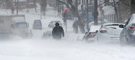 A blizzard with blocked cars, red lights and people walking in the snow