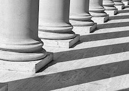 Pillars casting shadows on the ground in front of a courthouse