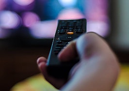 A hand holding a remote control pointed at a television